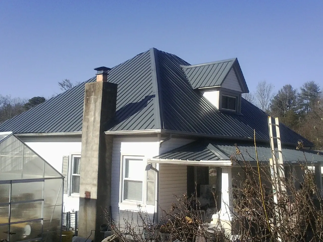 Dark blue standing seam metal roof on a white farmhouse with dormer — Slate & Tile Roof Repair by Roofing Brothers in New Site
