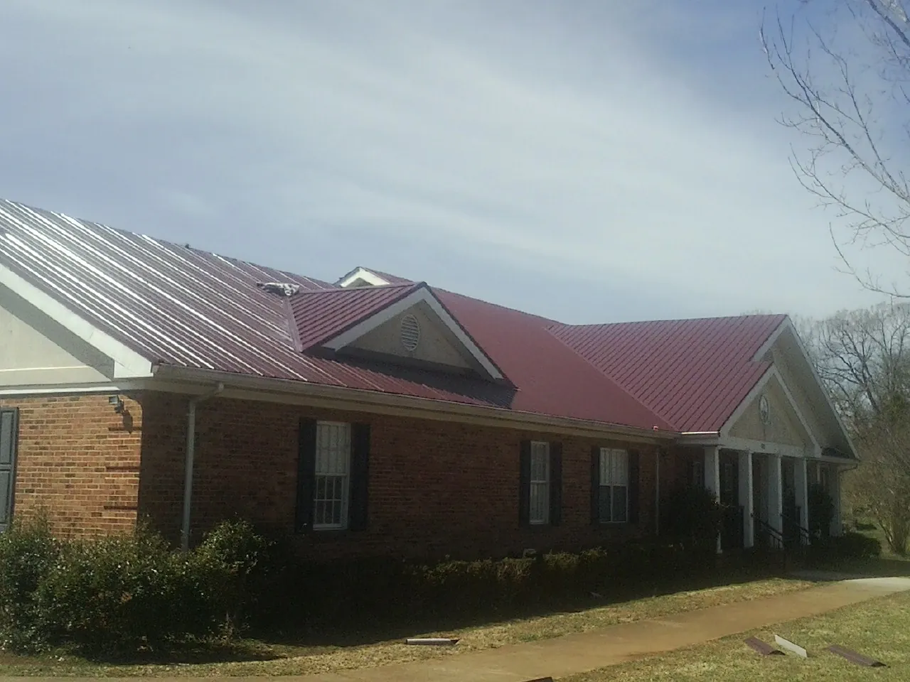 Red metal roof with gabled entries on a long brick building, from a Hail Damage Roof Repair job in New Site