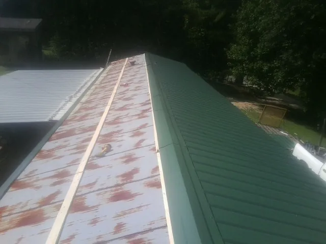 Old rusted panels beside newly installed green metal roofing — Wind Damage Roof Repair by Roofing Brothers in New Site
