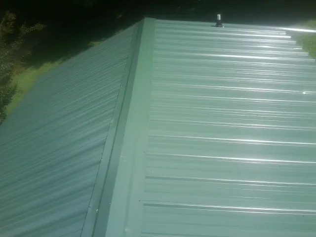 New green metal panels meeting at the ridge of a roof — Flat Roof Repair work by our crew in New Site