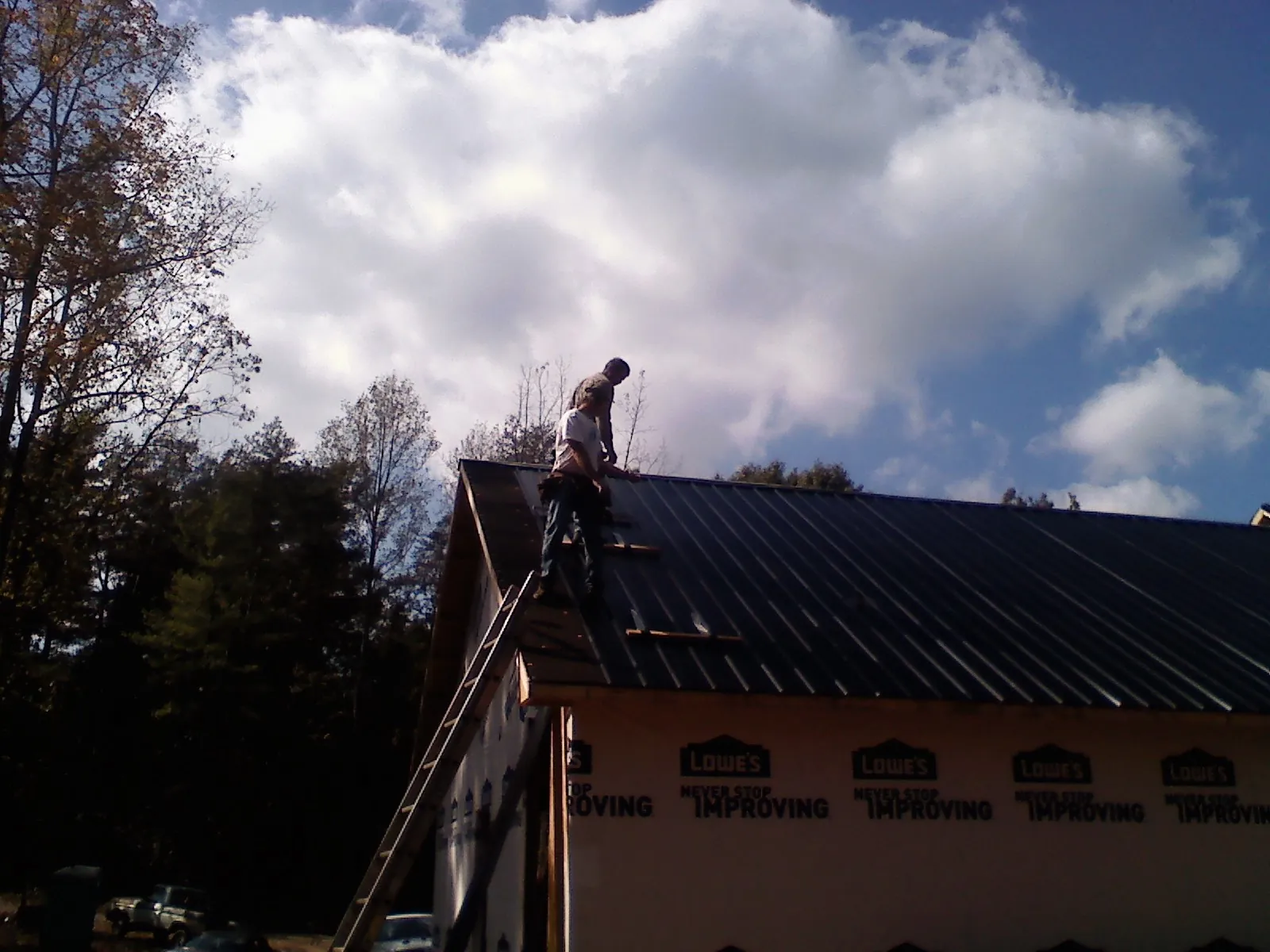 Roofer fastening dark metal panels high against a cloudy sky, from a Roof Inspection job in New Site