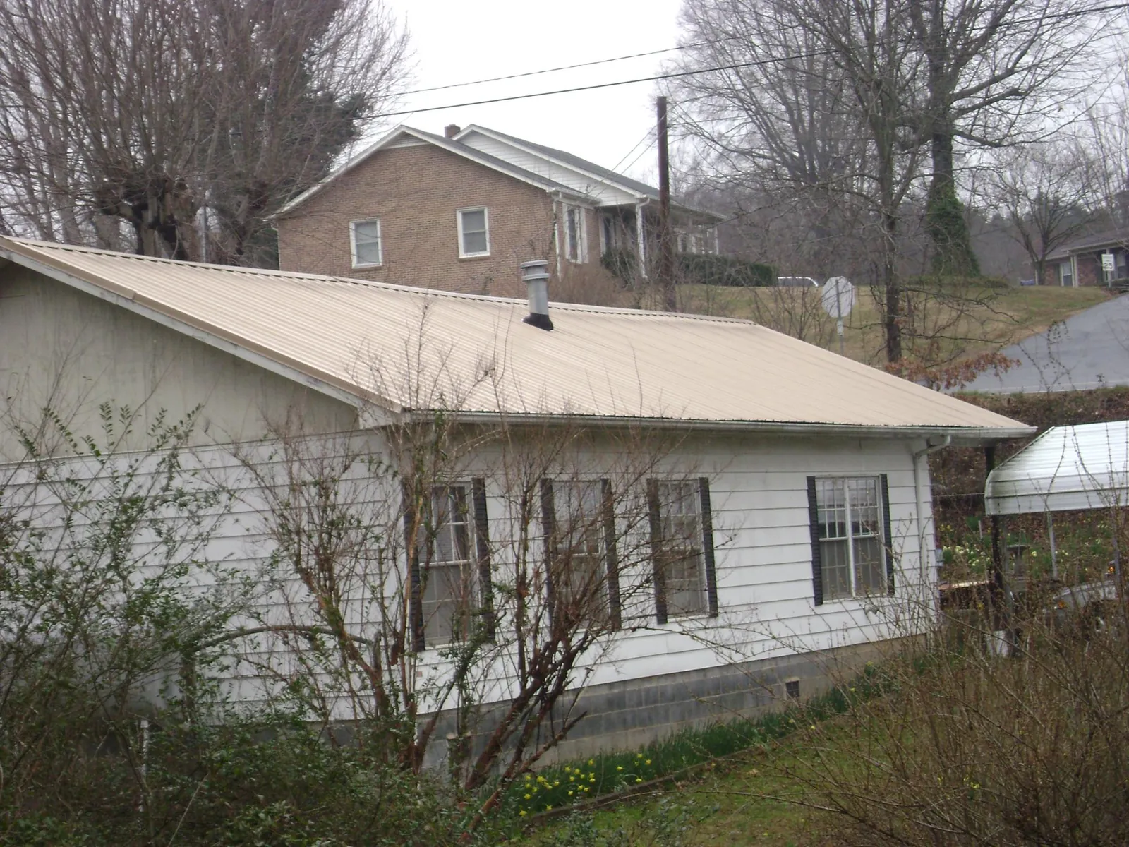 Tan metal roof on a white sided house set into a hillside — Commercial Roofing by Roofing Brothers in New Site